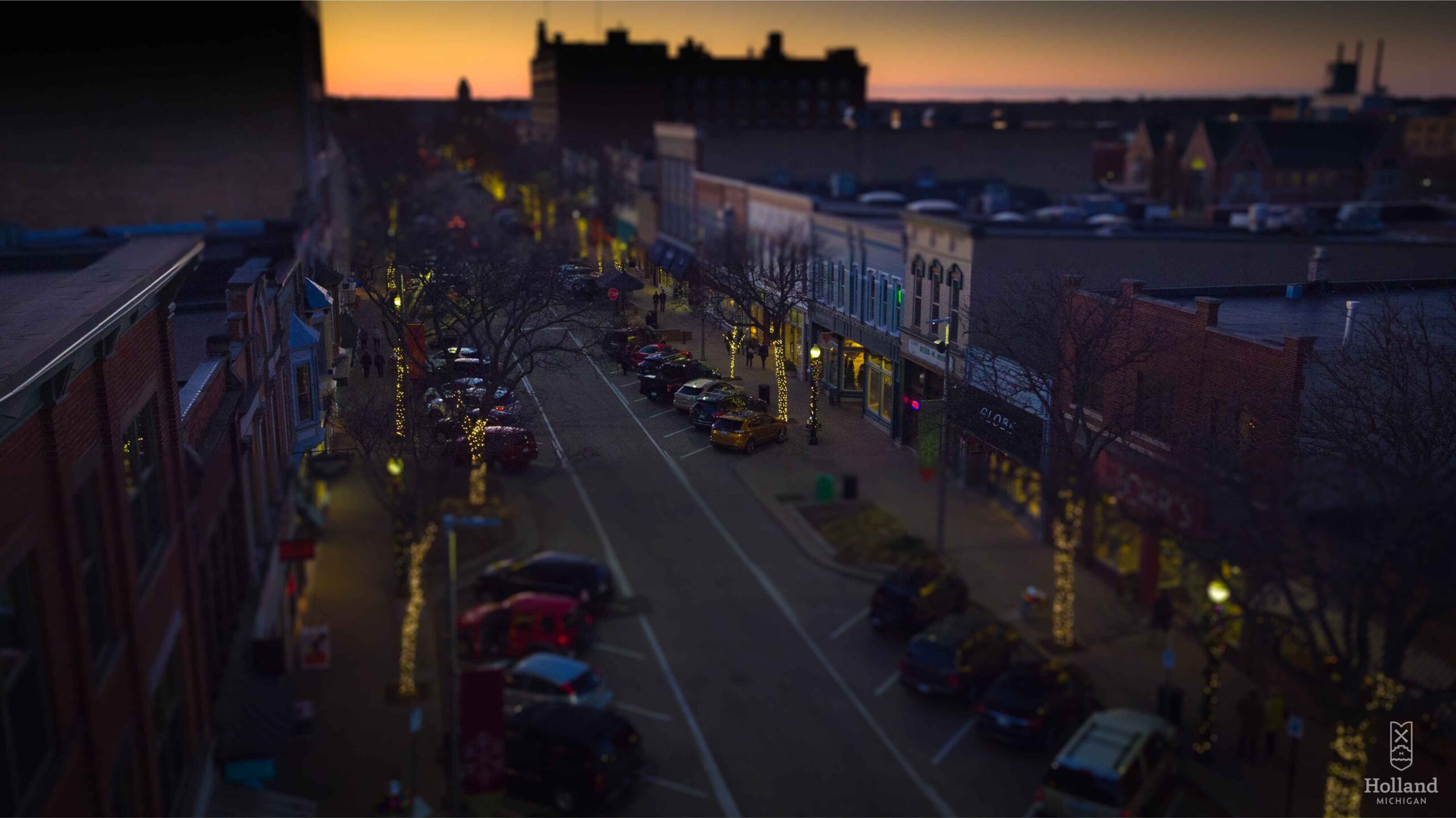 Downtown Holland Michigan glows with Christmas lights at dusk as trees and shops line the street during the town’s festive holiday season.