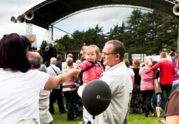 Families gather outdoors near a stage during the Kool Kat Hip Hop Panto at Theatre Nova enjoying live entertainment together