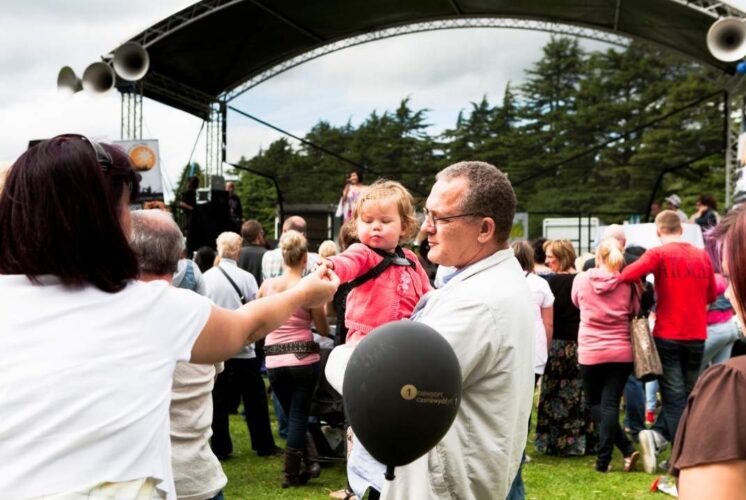 Families gather outdoors near a stage during the Kool Kat Hip Hop Panto at Theatre Nova enjoying live entertainment together