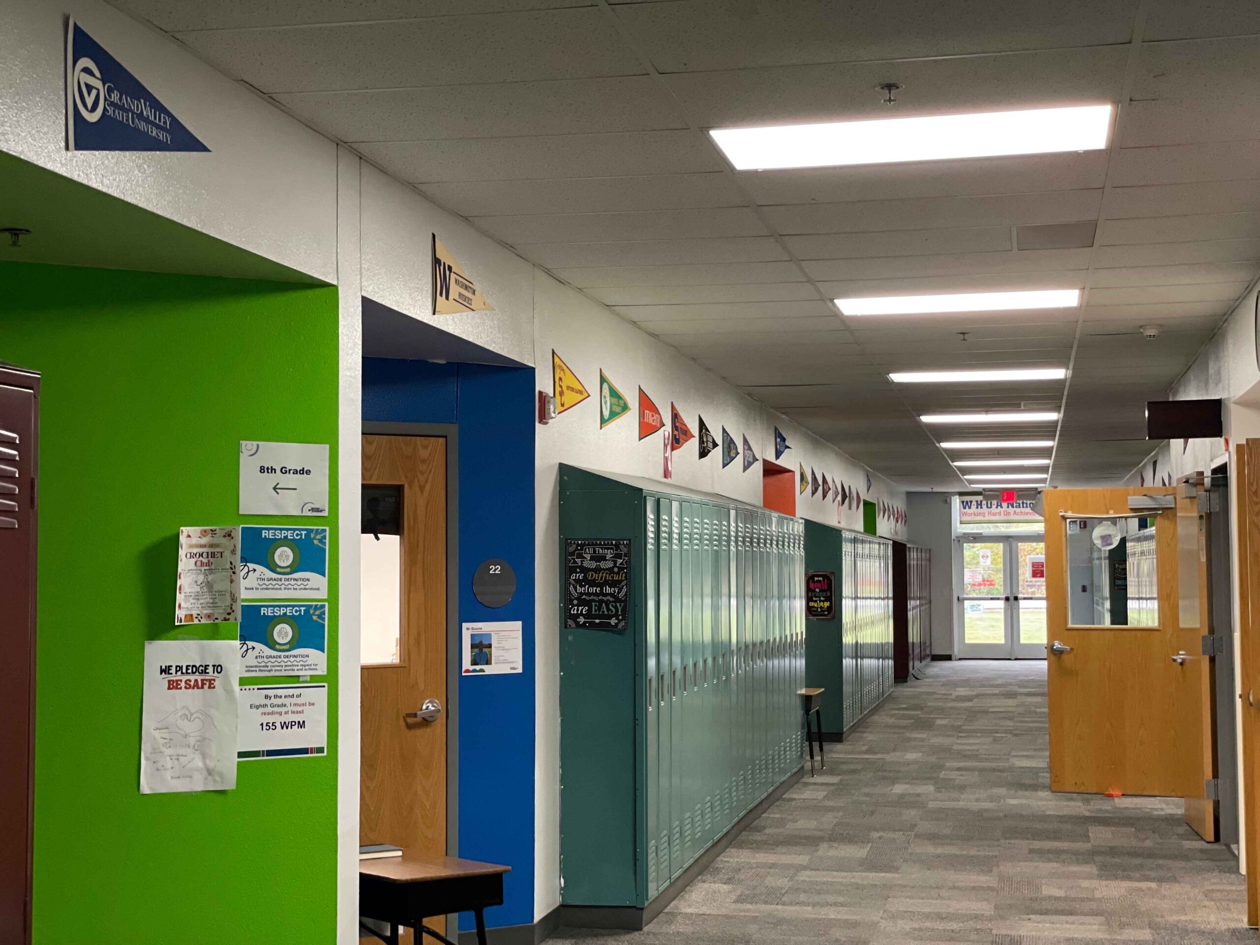 Hallway at Metro Charter Academy in Romulus, Michigan, featuring student lockers and college pennants, with signs promoting respect and reading fluency.