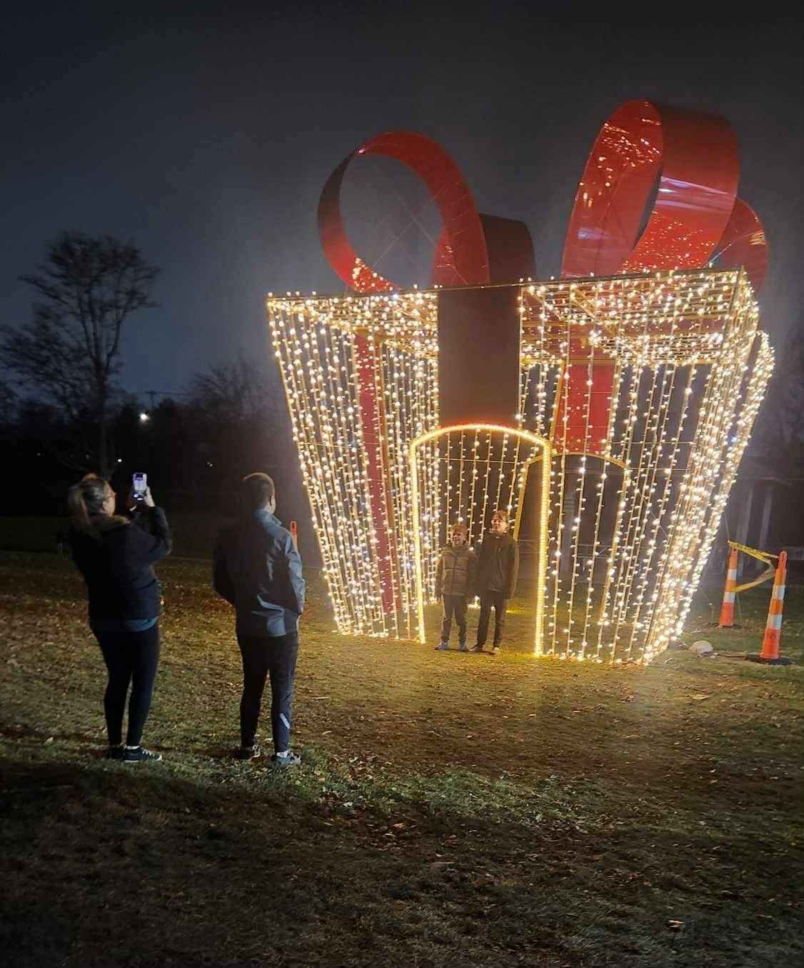 Families take photos inside a giant lighted gift box display at the Wayne County Lightfest in Westland Michigan.