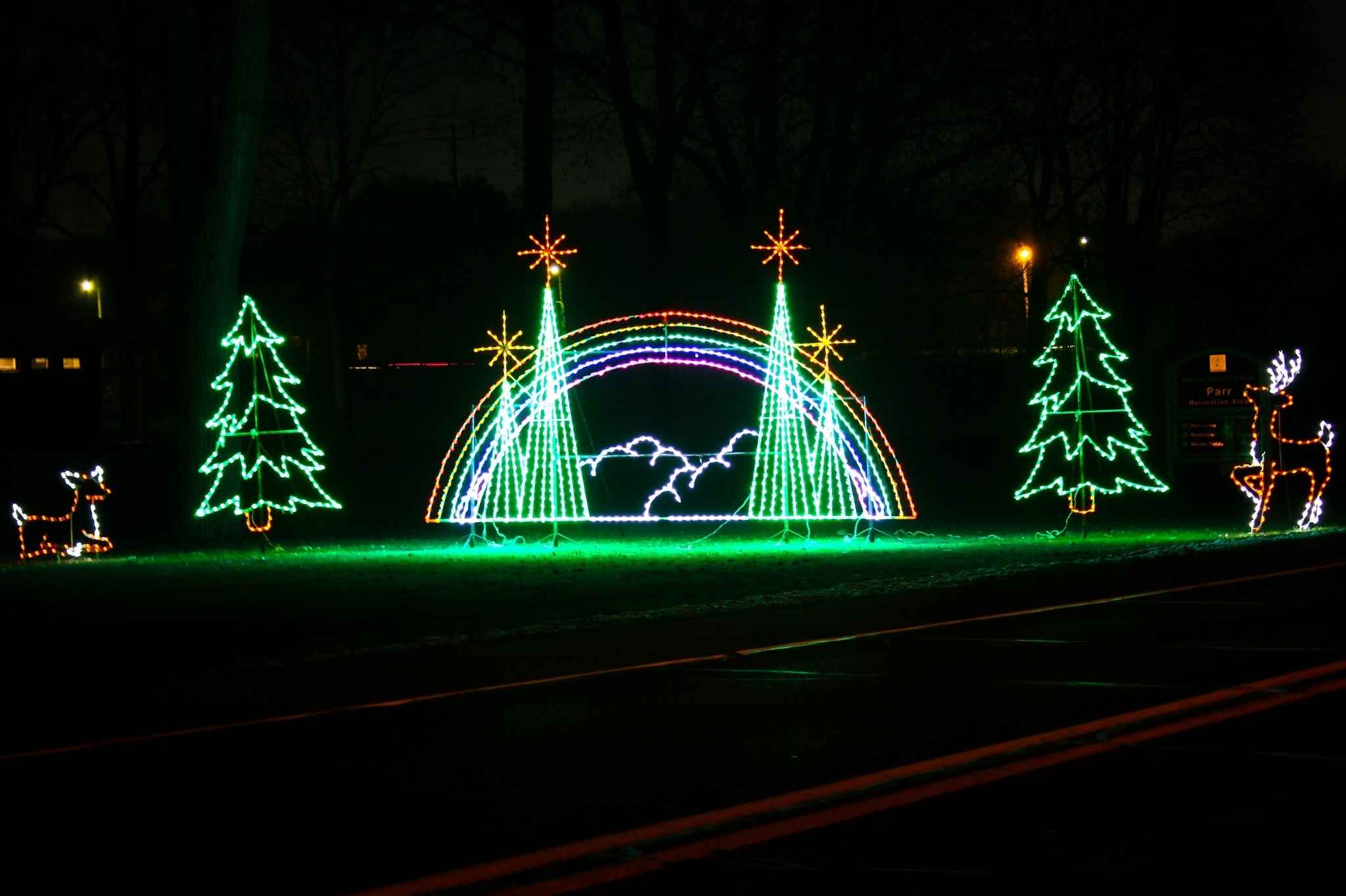 A colorful rainbow holiday light display glows along the Wayne County Lightfest route in Westland Michigan with trees and stars lit at night.
