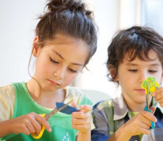Children cut paper during a craft activity similar to the Create Workshops at Decked Out Detroit where kids can enjoy creative hands on projects