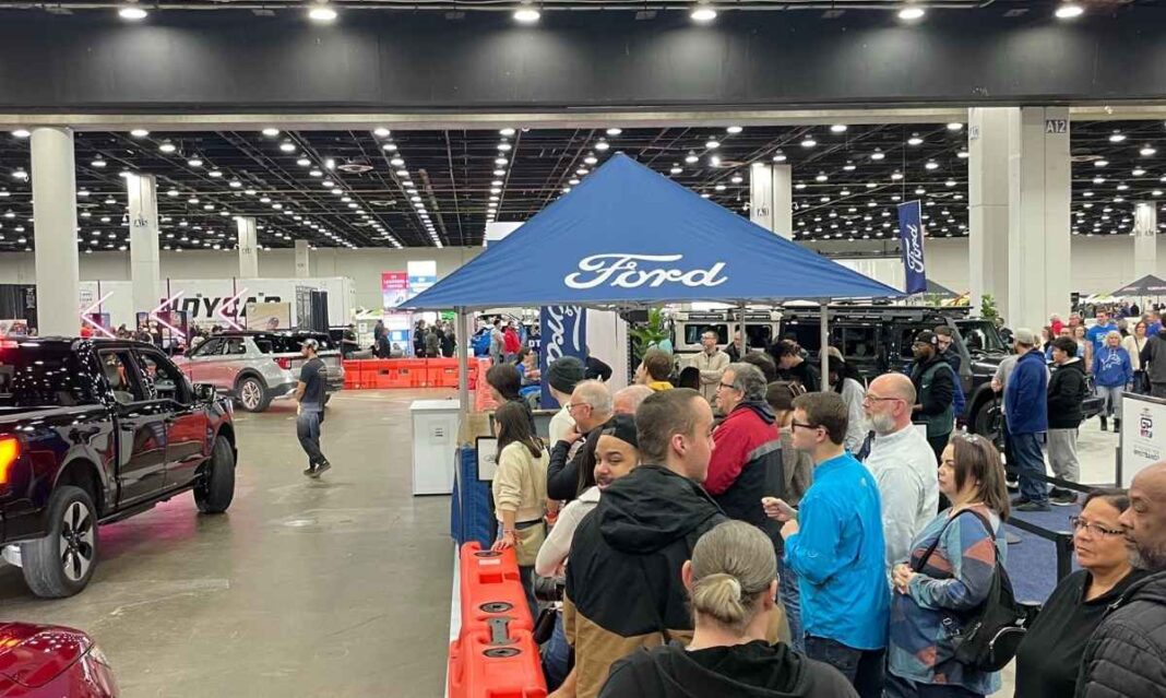 Detroit Auto Show Sweepstakes scene showing families gathered around a Ford exhibit at Huntington Place during the Detroit Auto Show.