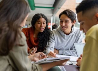 A group of diverse high school students collaborate at a table, smiling and reviewing notes together, representing the supportive and engaging environment of the Early College of Macomb program.