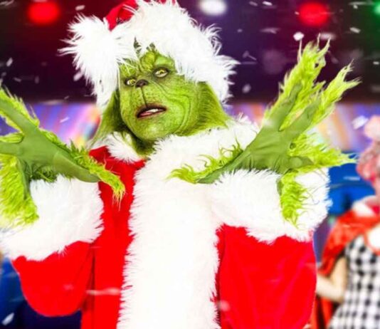 The Grinch And Cindy Lou Who Show at Fairytale Fun Place The Grinch in a Santa costume poses onstage during The Grinch And Cindy Lou Who Show at Fairytale Fun Place with festive lights in the background