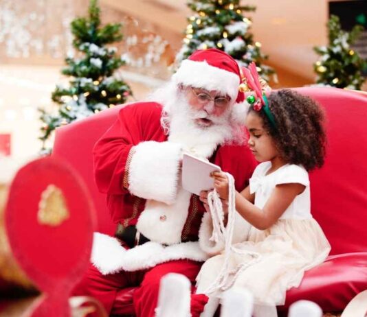 Santa Photo Experience at Briarwood Mall Santa sitting with a young child during Holiday magic at Greenmead as they look at a book together in a festive setting