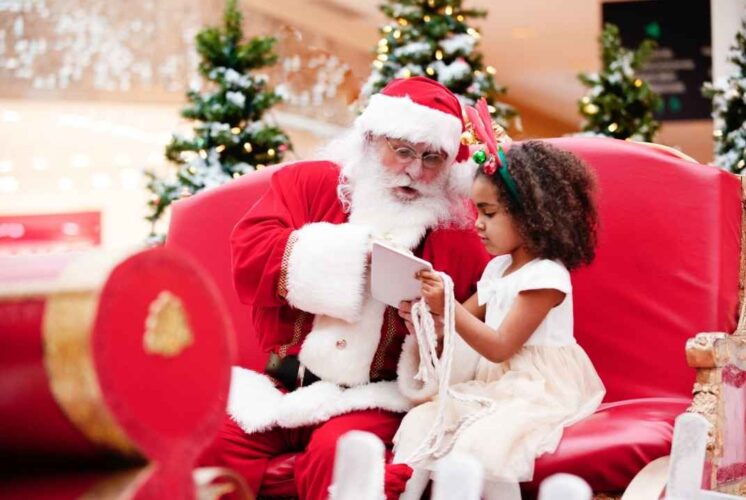 Santa sitting with a young child during Holiday magic at Greenmead as they look at a book together in a festive setting