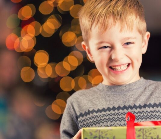 Holiday Sleigh of Giving at Southfield Public Library Child smiling and holding a gift at the Holiday Sleigh of Giving Southfield event with festive lights creating a warm holiday atmosphere