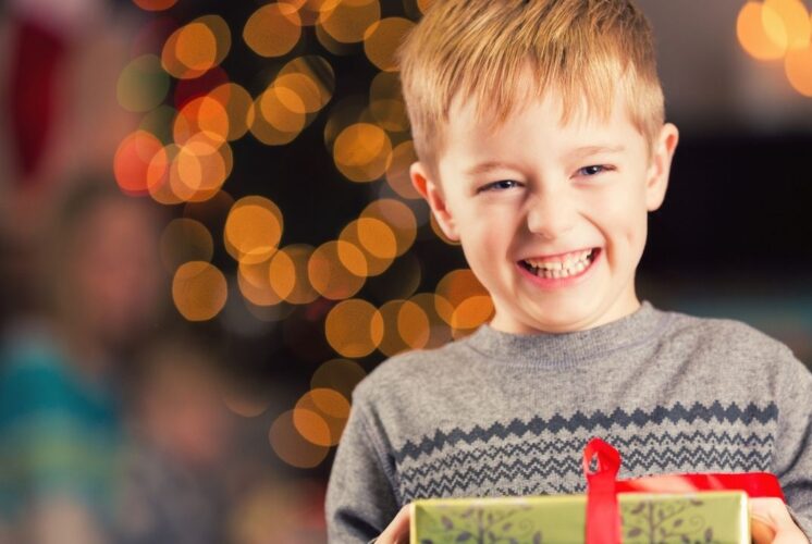 Child smiling and holding a gift at the Holiday Sleigh of Giving Southfield event with festive lights creating a warm holiday atmosphere
