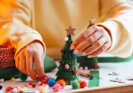 Hands decorate a small holiday tree with colorful pom poms during Hudson’s for the Holidays Detroit where families enjoy festive crafts