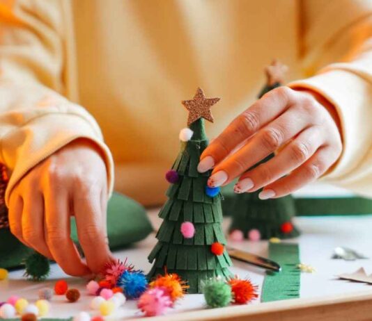 Hands decorate a small holiday tree with colorful pom poms during Hudson’s for the Holidays Detroit where families enjoy festive crafts