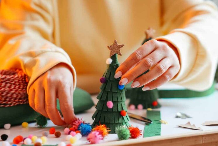 Hands decorate a small holiday tree with colorful pom poms during Hudson’s for the Holidays Detroit where families enjoy festive crafts