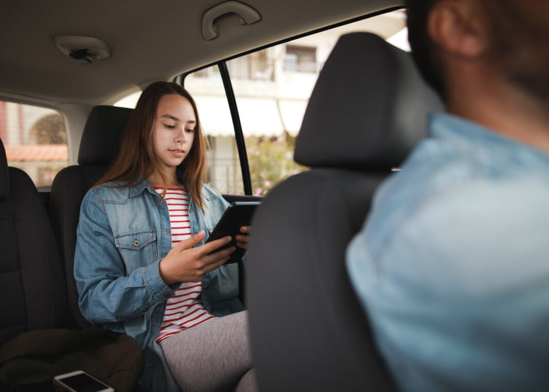 Photo of teenage girl typing on digital tablet in the taxi