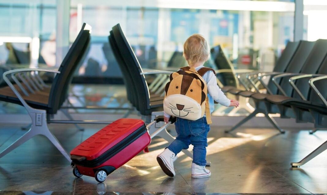Young child walking through an airport with a suitcase and backpack highlighting kids holiday travel health tips and staying healthy on the go