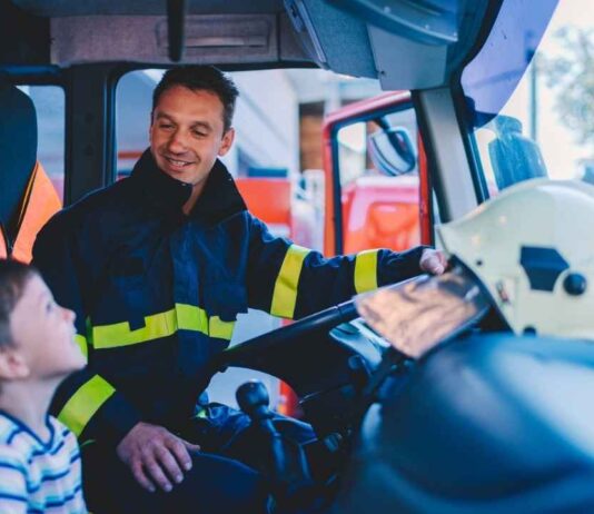 Lights, Sirens and Heroes Night at Greenmead Historical Village Firefighter showing a fire truck to a child during Lights Sirens and Heroes Night at Greenmead Historical Village for a family friendly event