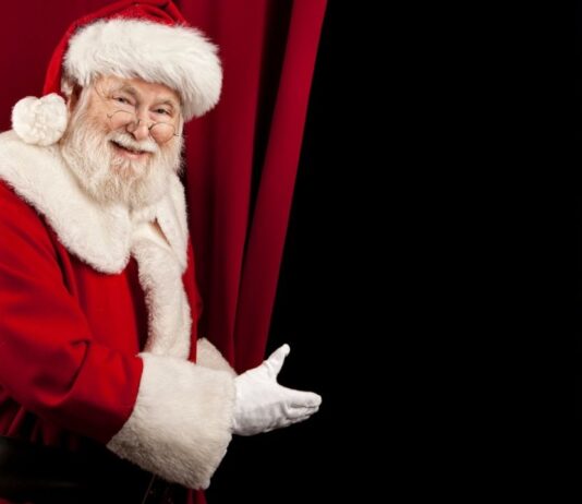 Miracle on 34th Street at the Fox Theatre Santa smiles and gestures toward a stage curtain promoting the Miracle on 34th Street show at the Fox Theatre supporting Make-A-Wish Michigan