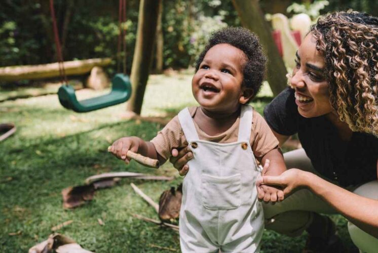 Toddler smiling with a caregiver outdoors for Rock Around the Hawk Farmington Hills as little ones enjoy playful music inspired activities
