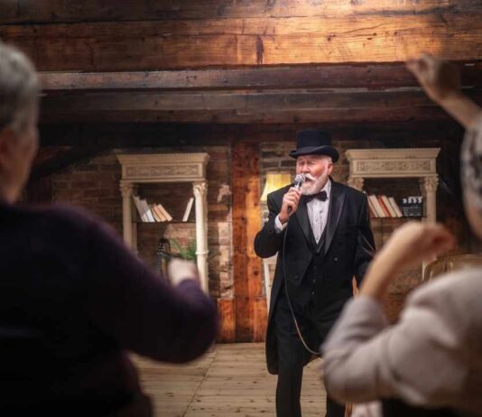 Scrooge at The Hawk Theatre Performer dressed as Scrooge sings onstage at The Hawk Theatre as audience watches during a family friendly holiday show