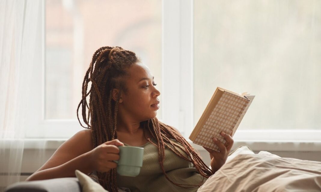 A mother taking time for self-care, relaxing at home with a book and a warm drink—an example of mindfulness for autism caregivers.