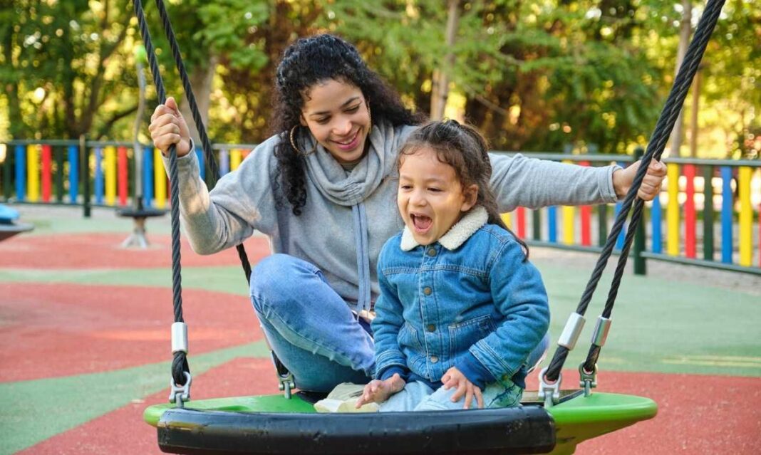 A parent supports a child on a playground swing, illustrating how guidance and predictability can help children with autism navigate transitions.