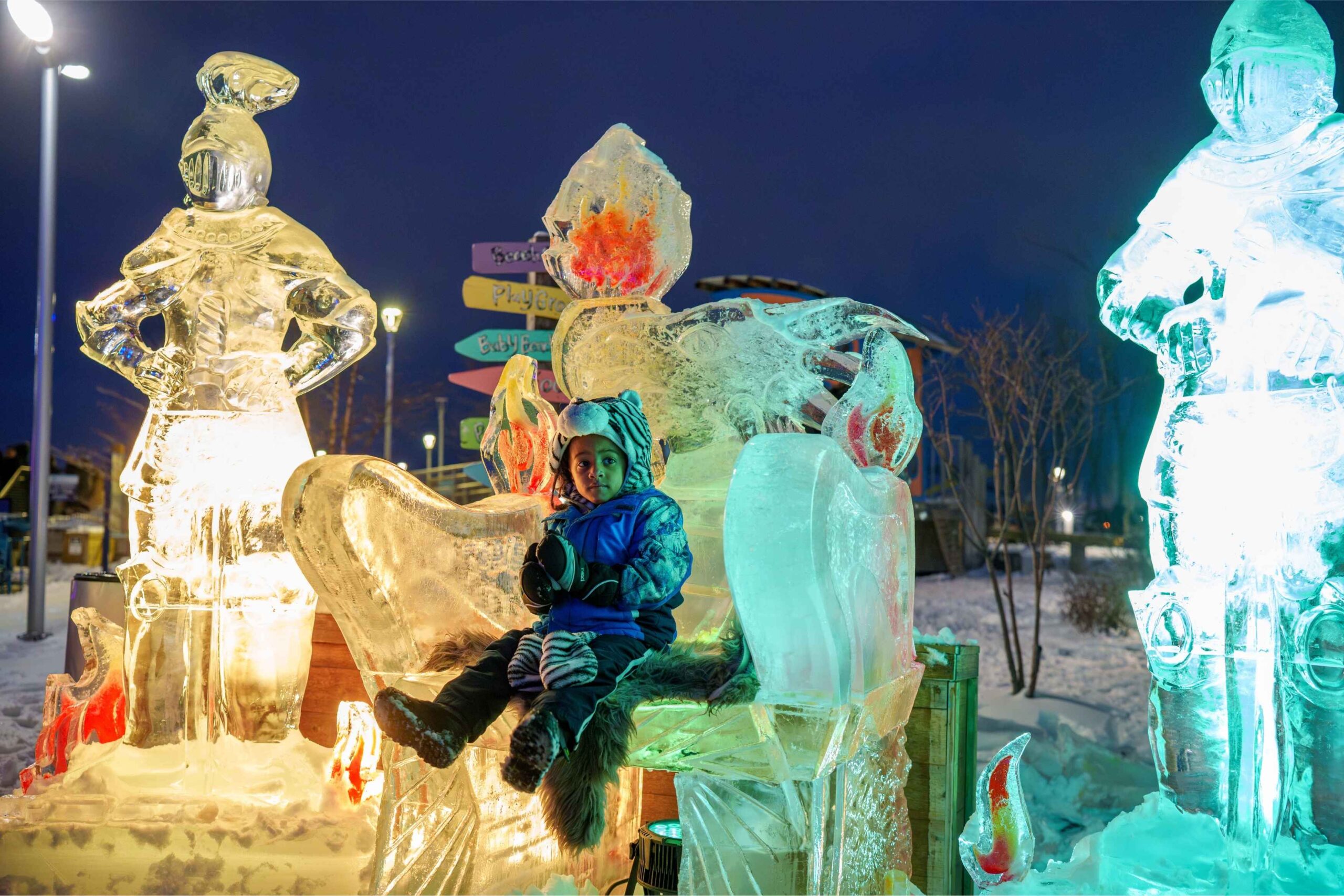 A child sits on an ice throne during the Fire and Ice Festival at Robert C Valade Park with glowing ice sculptures and winter fun