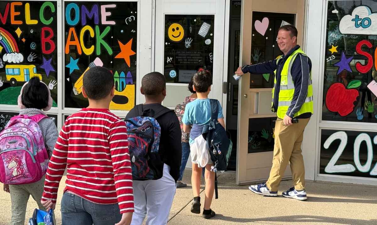 Students arrive at a Livonia Public Schools building on the first day of school, greeted by staff at a decorated entrance welcoming families back.