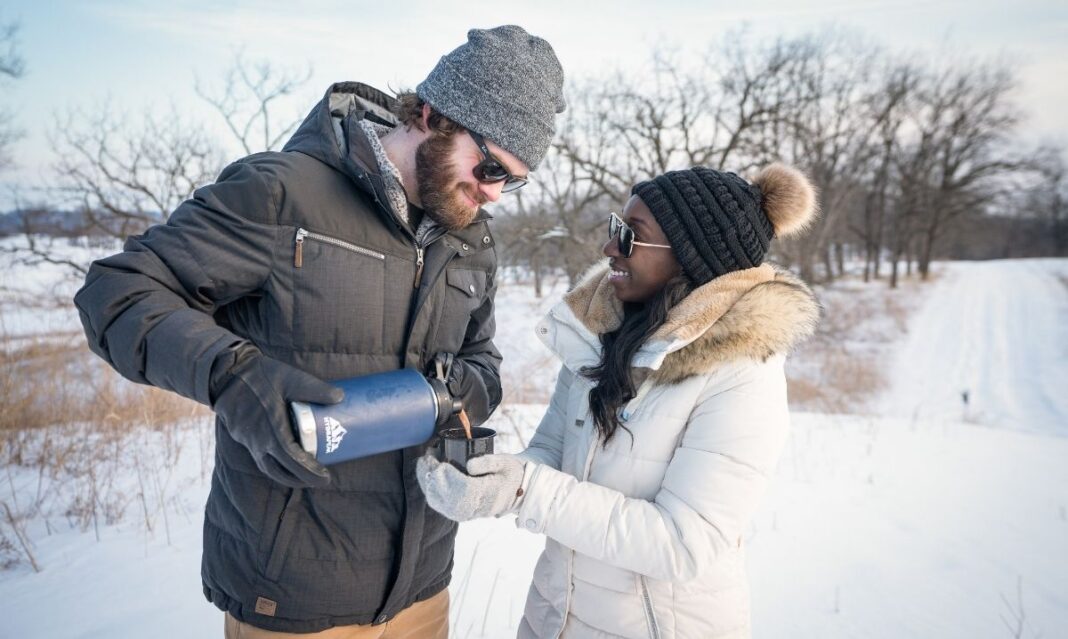 Couple enjoying a winter road trip near Metro Detroit, sharing a hot drink outdoors during a Midwest winter getaway with snowy scenery