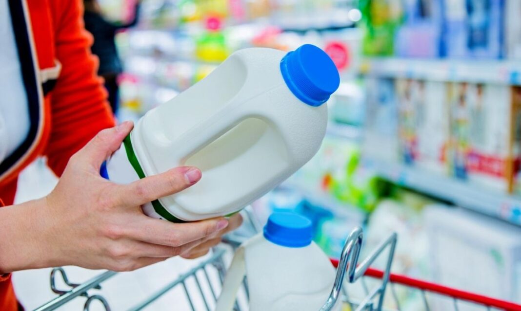 Parent holding a gallon of pasteurized milk while shopping in a grocery store dairy aisle, choosing milk for their family.