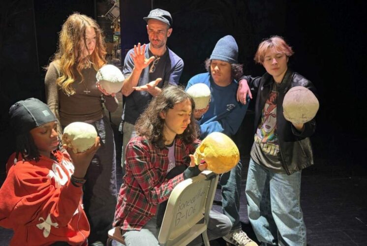 PTG presents Hamlet Pioneer High School student cast holding skull props on stage during a modern theater production rehearsal