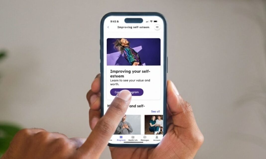 Close-up of a person using the Teladoc Health app on a smartphone, selecting the “Improving your self-esteem” program for self-guided mental health support
