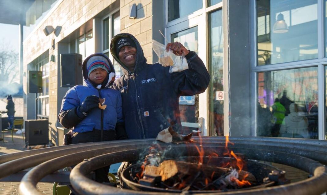 Family warms up by a bonfire during Winter at Valade at Robert C Valade Park with free weekend winter fun along the riverfront