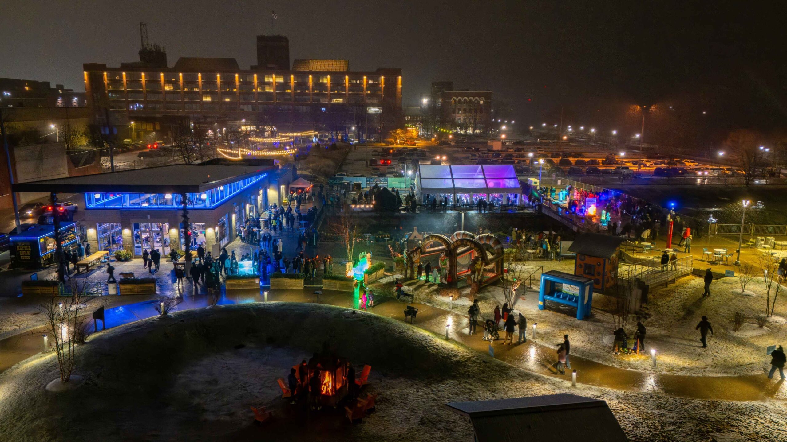 A nighttime view of Winter at Valade at Robert C Valade Park with families enjoying lights, bonfires and winter activities along the riverfront