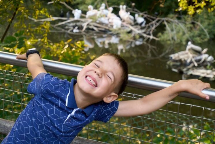 Preschool child enjoying Zoo Tots animal habitats program while exploring a zoo habitat with birds and water behind him
