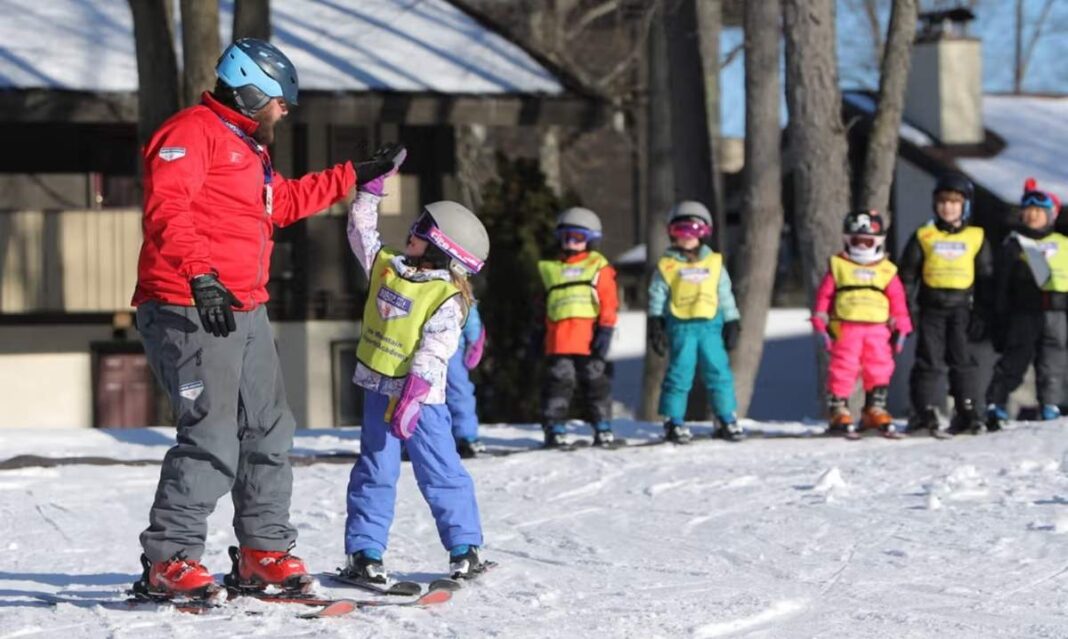 Ski instructor high fives child during ski lesson at Boyne Mountain in Boyne Falls, Michigan on a winter family getaway.