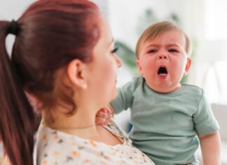 Mother holding a baby who appears to be coughing indoors