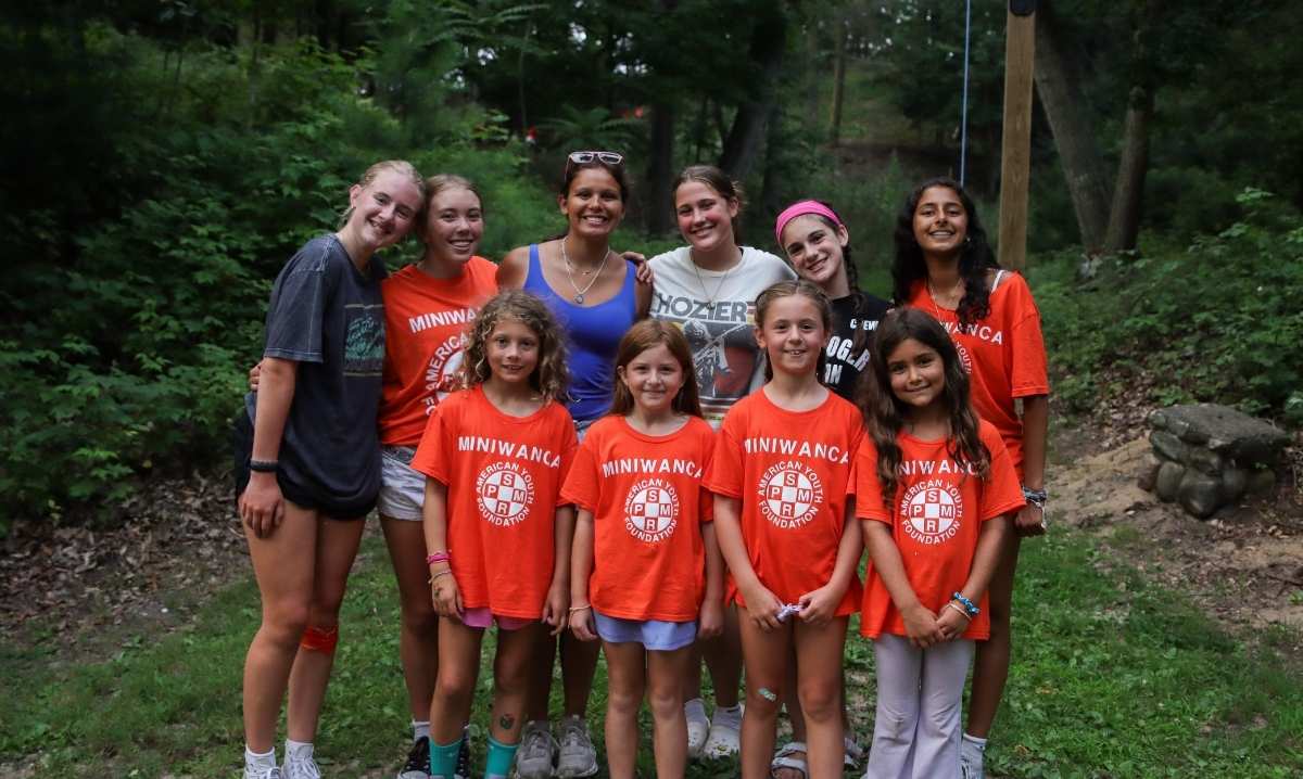 Camp Miniwanca campers pose together outdoors in matching shirts during summer camp in a wooded setting.