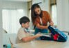 Parent helping child with autism pack backpack and get ready for school as part of morning routine