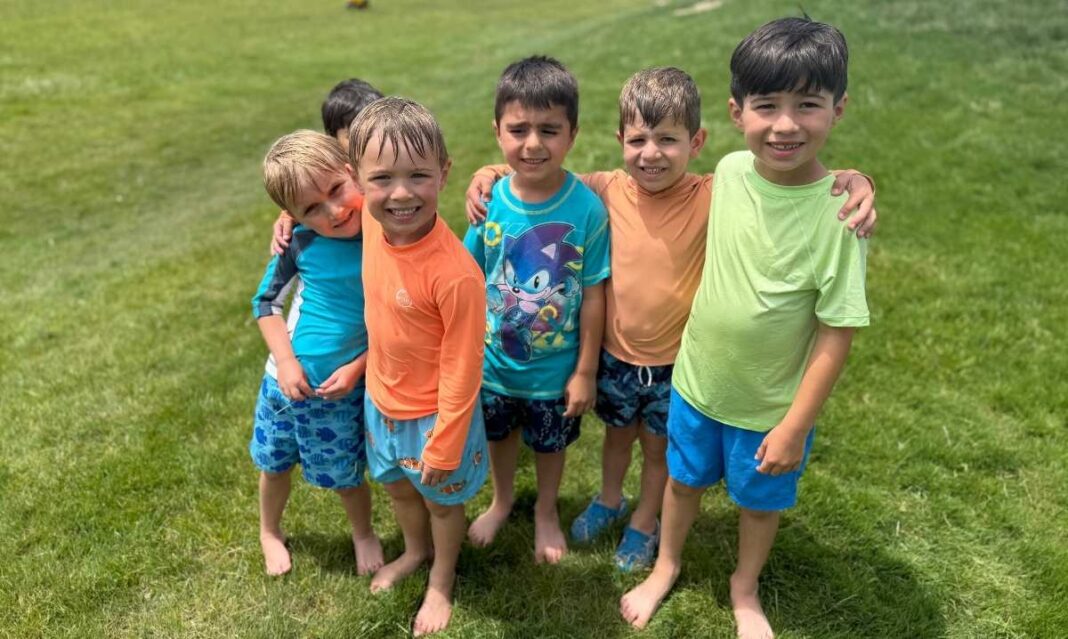 Group of kids stand together on grass during outdoor activities at Detroit Country Day Camps, showing teamwork, play and summer fun