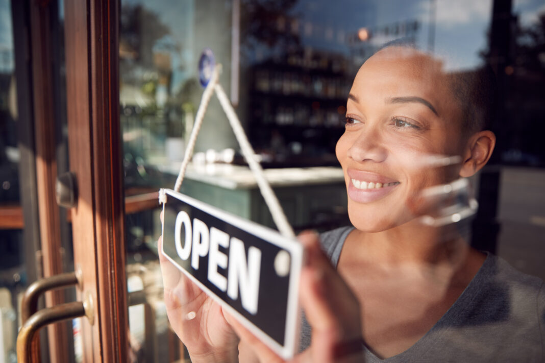 Female Owner Of Start Up Coffee Shop Or Restaurant Turning Round Open Sign On Door. Women business