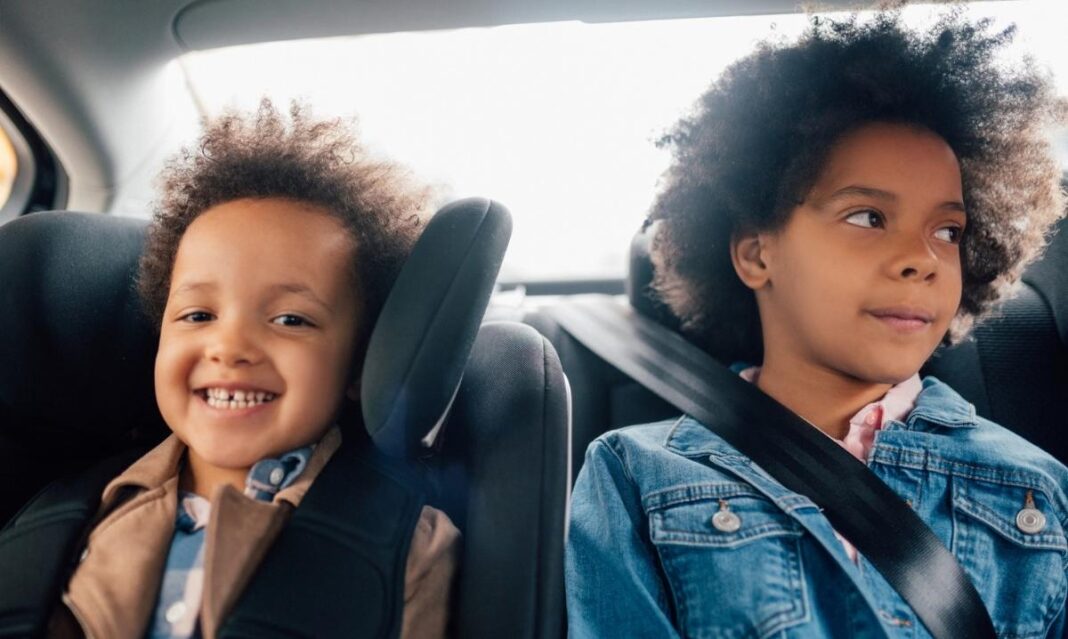 Two young children riding in the back seat of a car during a road trip, illustrating travel tips to help prevent motion sickness in kids.
