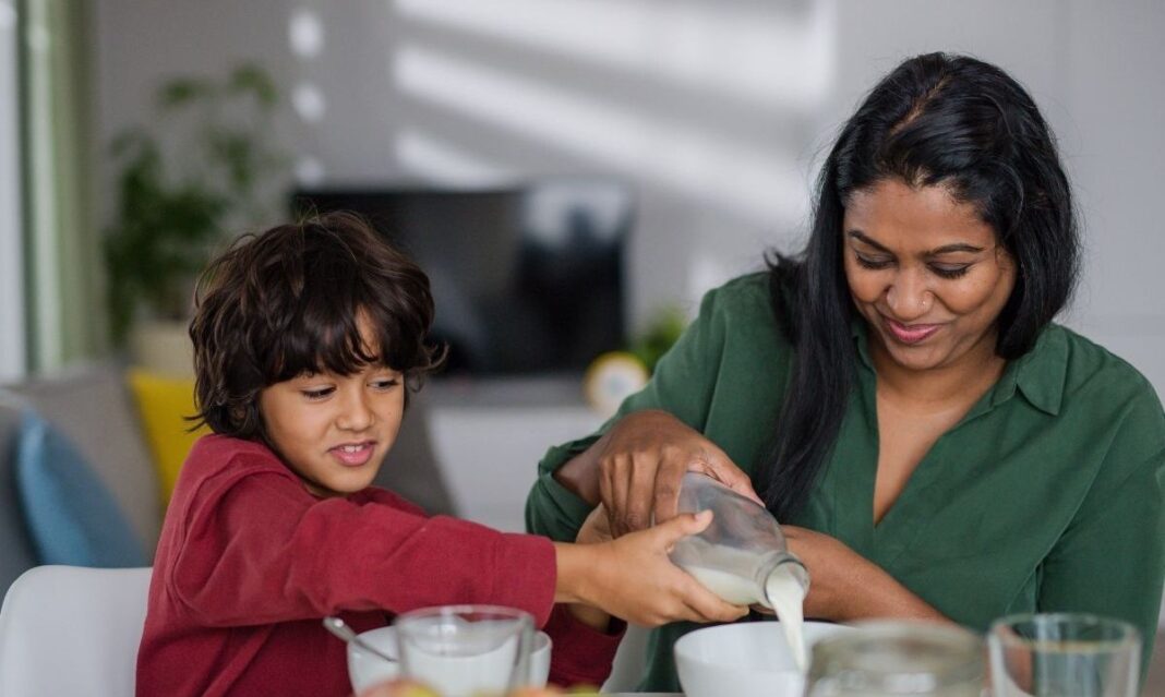 Family eating breakfast together with cereal, milk, yogurt and fruit at the kitchen table.