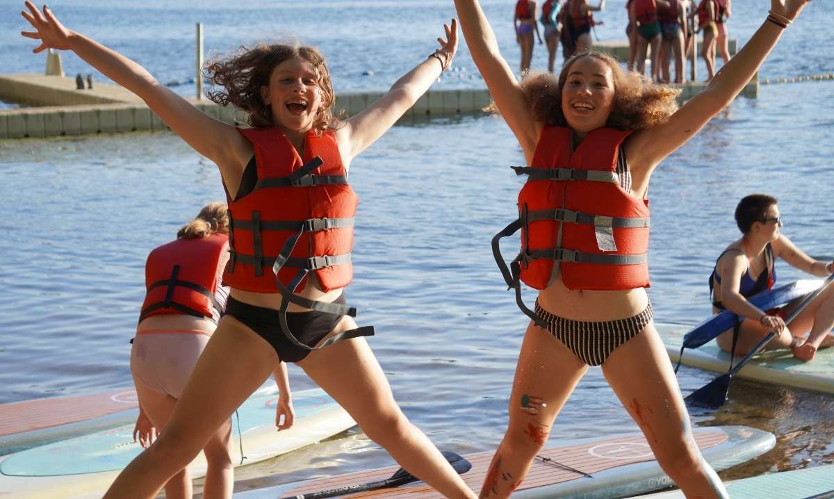 Girls at YMCA Camp Arbutus Hayo-Went-Ha jump with excitement during paddleboarding on Arbutus Lake in Traverse City Michigan
