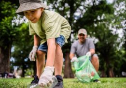 Child picking up trash during an Earth Day cleanup at a park with a parent helping, showing kids caring for the environment outdoors