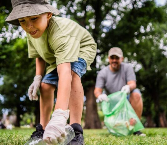 Child picking up trash during an Earth Day cleanup at a park with a parent helping, showing kids caring for the environment outdoors