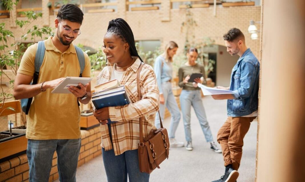 Diverse college students studying together on campus using a tablet and textbooks while walking between classes