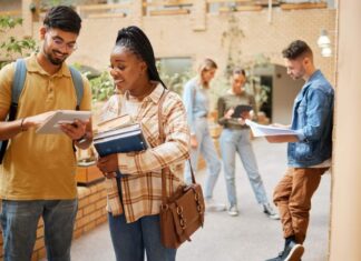 Diverse college students studying together on campus using a tablet and textbooks while walking between classes
