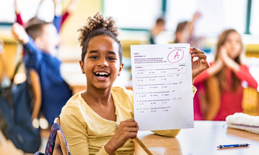 Elementary student smiling and holding an A graded test in a classroom, showing academic success and achievement