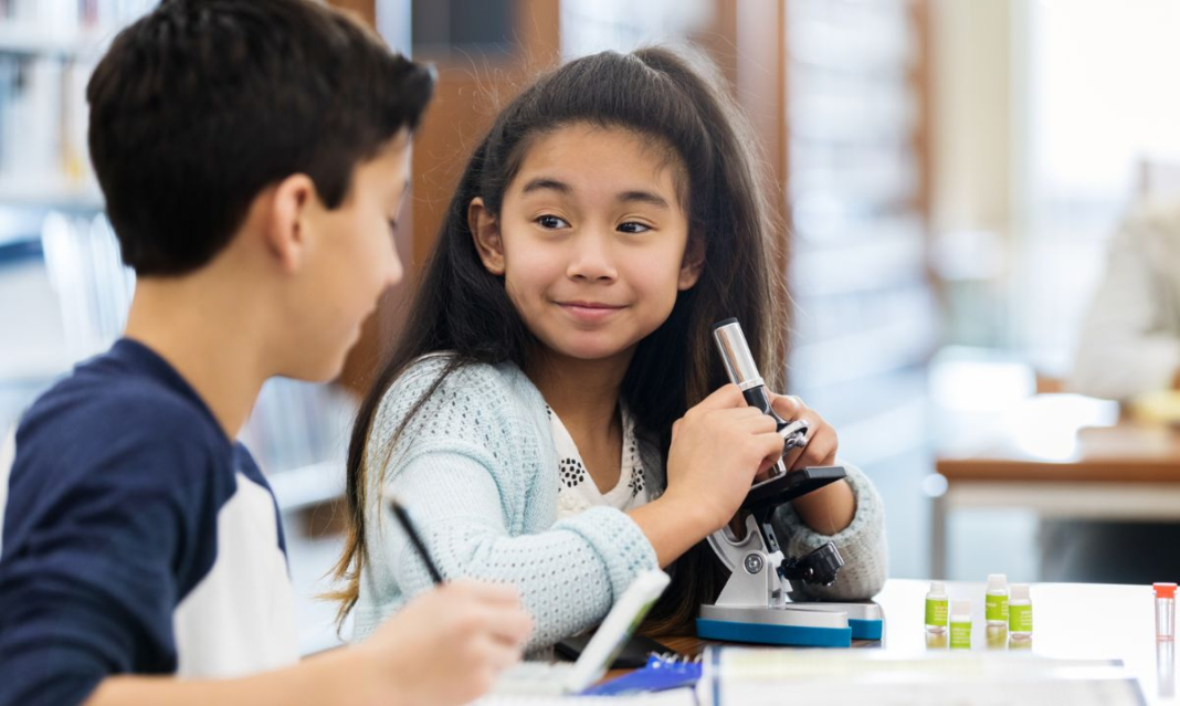 Elementary school students using a microscope in a classroom, exploring STEM learning through hands-on science activities