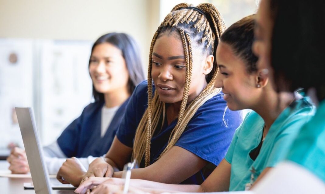 Nursing students collaborating on a laptop in a classroom, working together on coursework and training